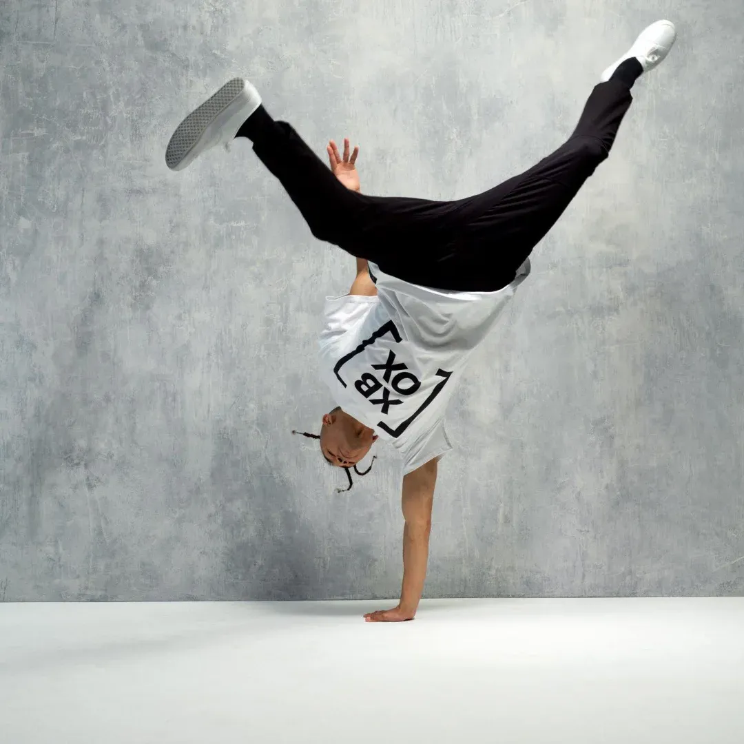 A man doing a handstand in front of a wall, wearing a white t-shirt, black pants, and white shoes.
