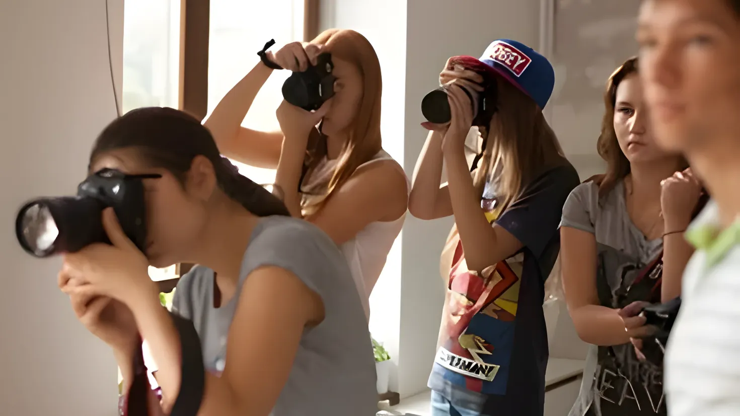 A group of people standing around each other, each holding a camera in their hands. In the background, there is a wall and a glass window.