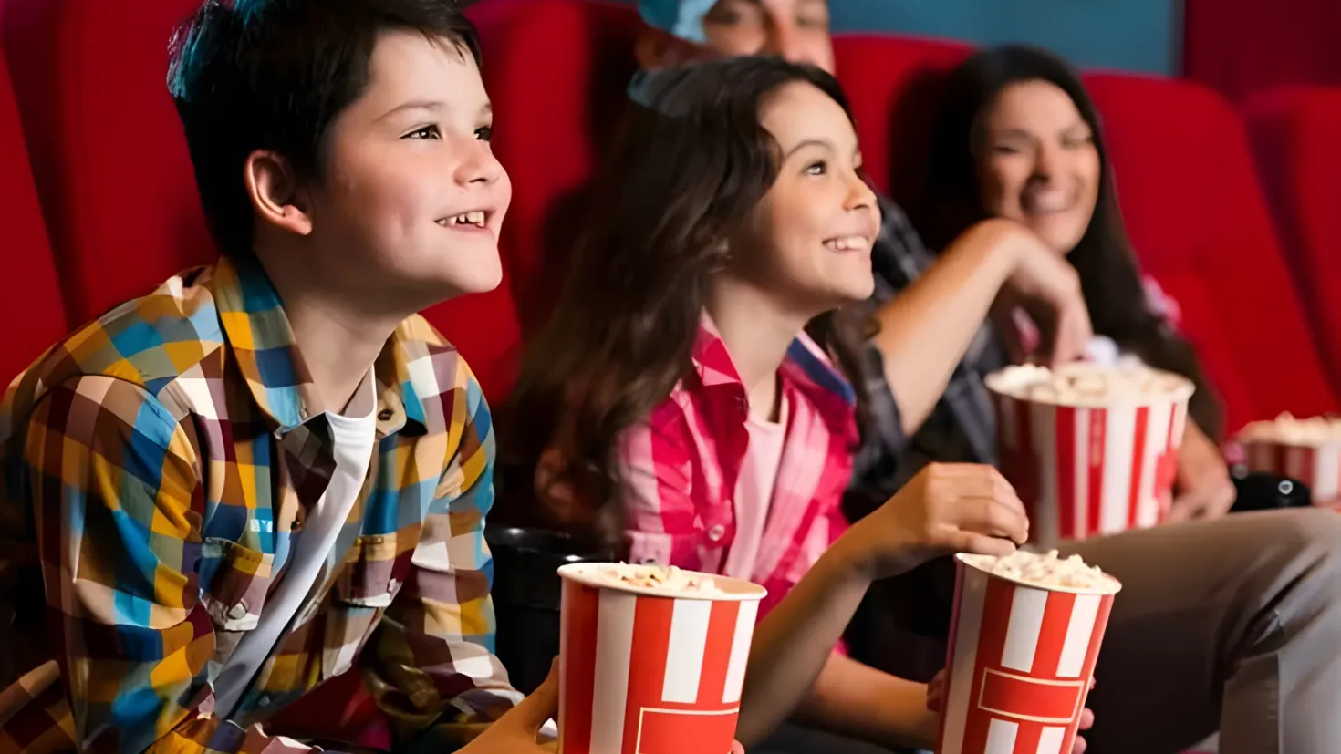 A group of people sitting in a movie theater, with popcorn buckets in their hands. They are all smiling and appear to be enjoying the movie.