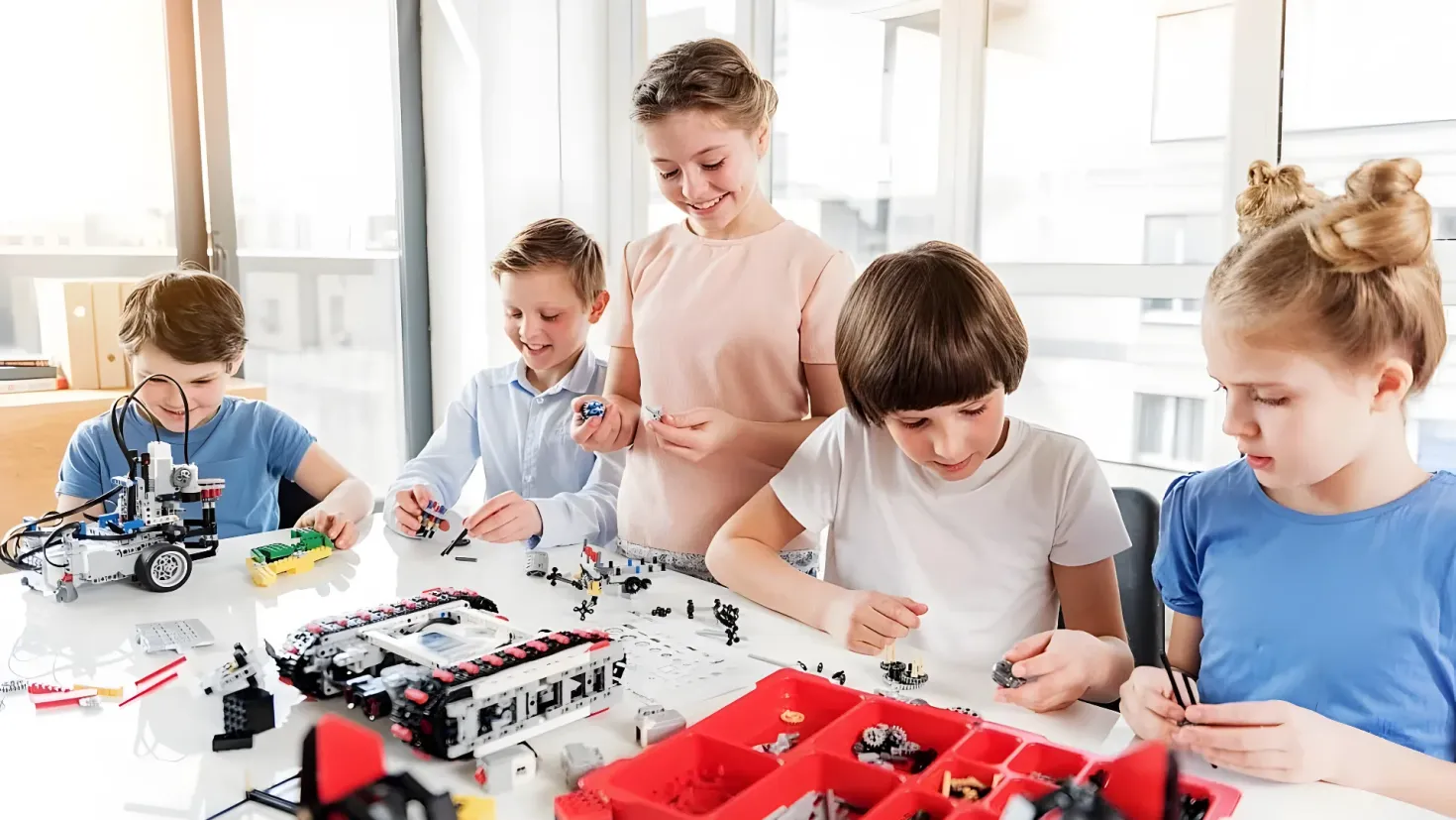 A group of children sitting around a table playing with legos. On the table there are various objects, and in the background there are glass windows.