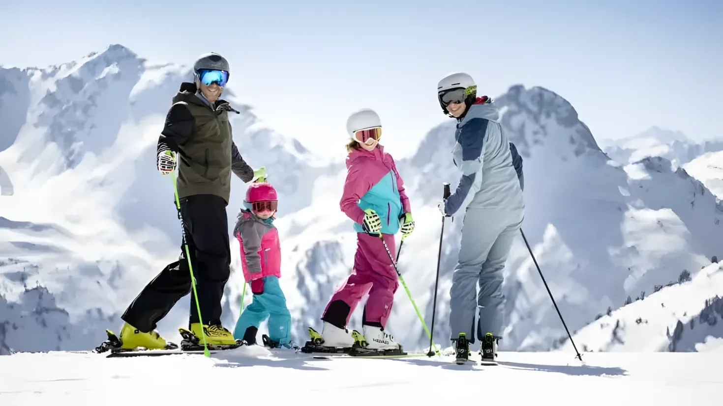 A group of people standing on top of a snow covered slope, each holding a ski pole. They are all wearing jackets, helmets, gloves, and shoes, and the sky is visible in the background.