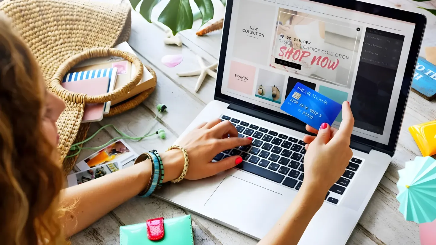 A woman sitting at a table with a laptop computer in front of her. She is holding a credit card in her hand and there are various items on the table such as a hat, books, a wallet, a mobile phone, and other objects. There are also leaves and other items scattered around the table.
