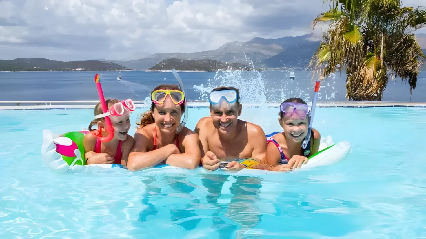 A group of people in a swimming pool with snorkeling gear, including goggles, swimming tubes, and a life saver. The pool is surrounded by a railing and there is a tree in the background, with hills and a sky with clouds in the distance.