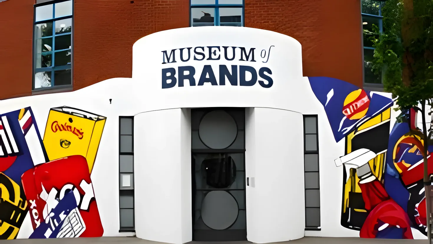 A building with windows and a door, a sign that reads "Museum of Brands" on the side of it, a tree to the right, and a sky in the background.
