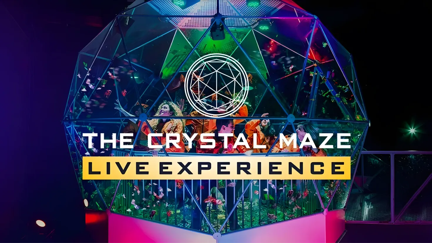 A group of people standing in front of a crystal maze, illuminated by lights and surrounded by a railing. The text on the image reads "The Crystal Maze Live Experience".