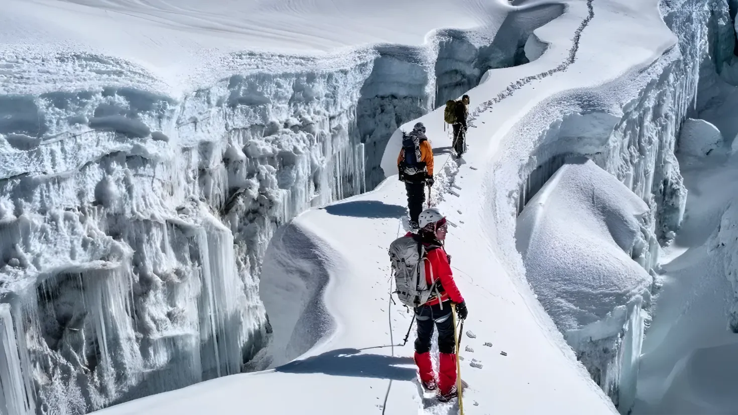 A group of people walking up a snowy mountain side, each wearing a backpack and holding ski poles. The snow is glistening in the sunlight, and the mountains in the background are covered in a blanket of snow.