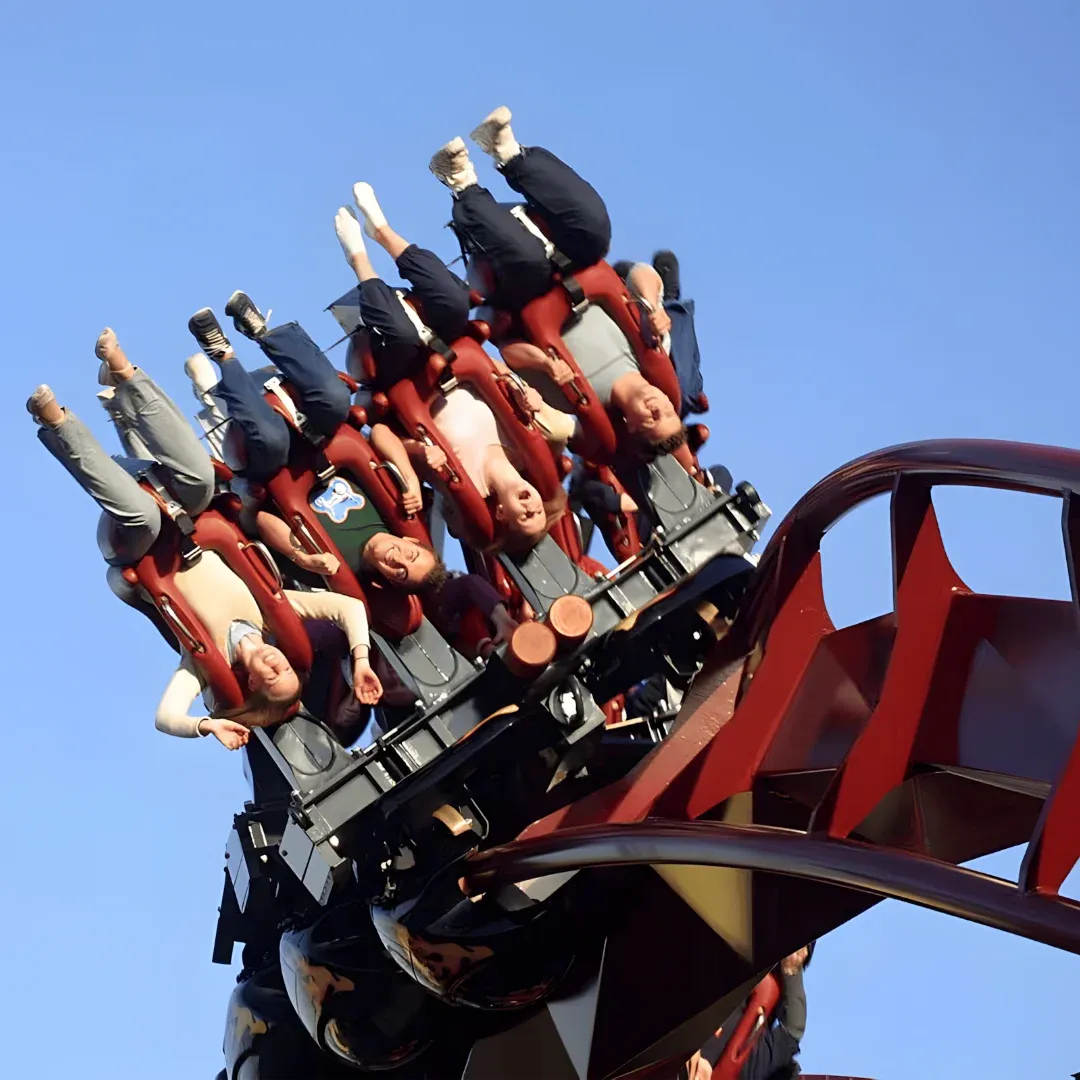 A group of people riding on top of a roller coaster, with a bright blue sky in the background. The roller coaster is part of the Six Flags Magic Mountain theme park, and the people are enjoying the thrill of the ride.