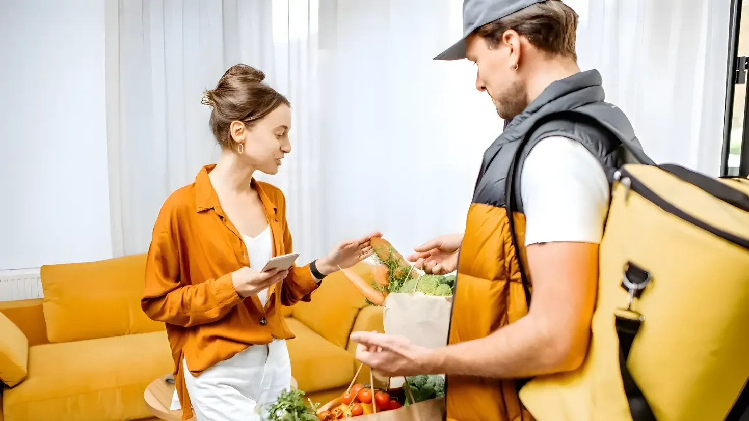 A family of three - a man, woman and a little girl - shopping in a grocery store. The man is pushing a trolley filled with fruits and vegetables, while the woman and girl are standing beside him. On the right side of the image, there are shelves filled with various food items, and on the left side, there is a pineapple. The background is slightly blurred, and there are lights attached to the ceiling.
