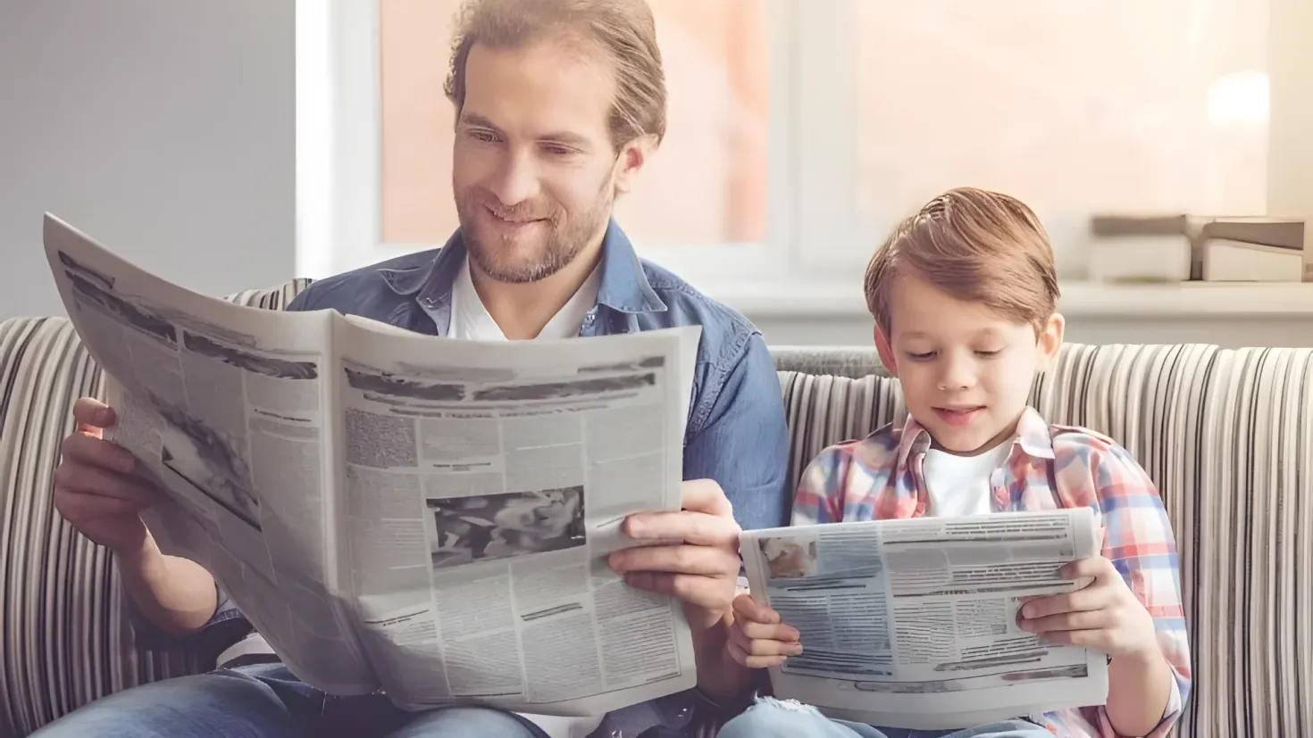 A father and son sitting on a couch, both of them reading a newspaper together. The father is holding the newspaper in his hands, while the son is looking intently at it. In the background, there is a wall and a window, and on the right side of the image, there are some objects on a platform.