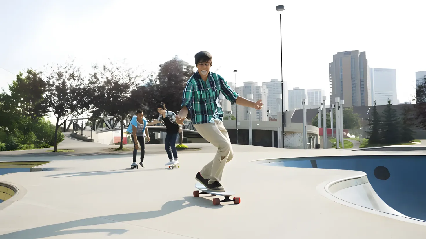 A group of people riding skateboards down the side of a ramp, surrounded by street light poles, trees, buildings, and a clear blue sky.