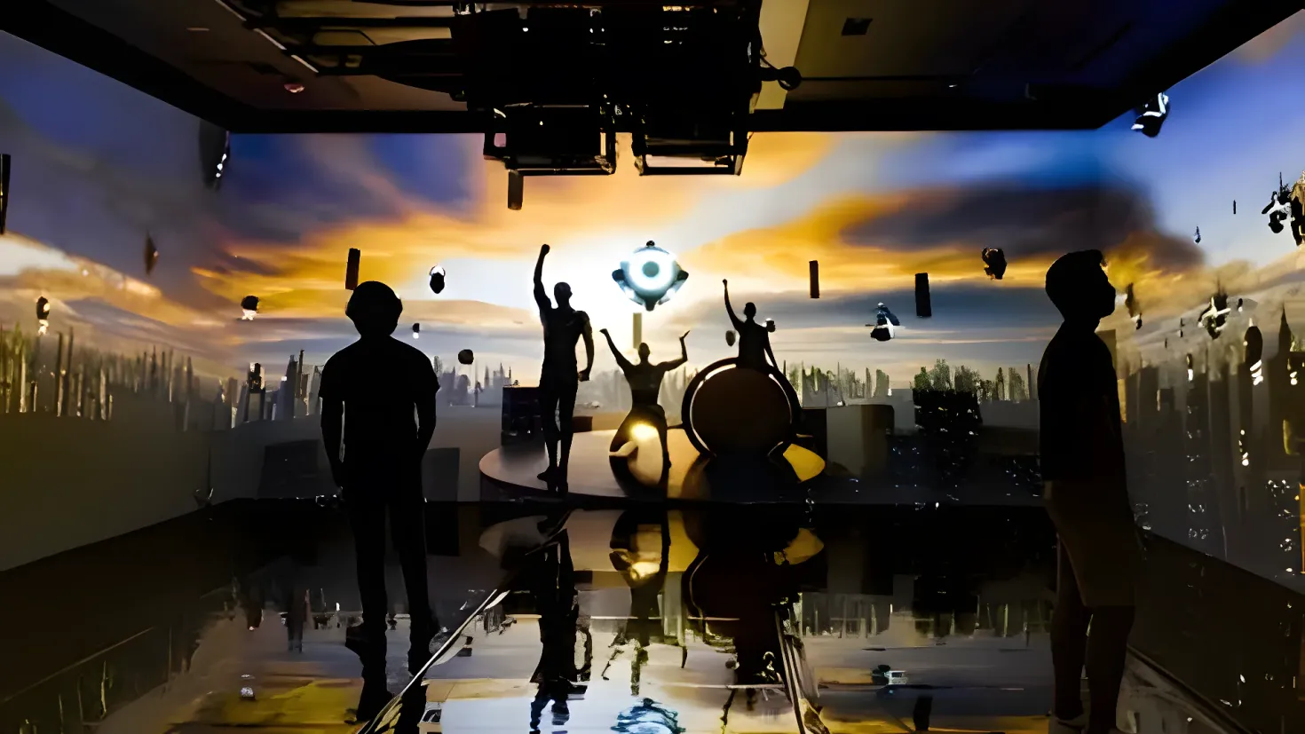 A group of people standing on top of a stage, illuminated by lights attached to the ceiling. In the background, there are buildings, trees, and a sky with clouds.