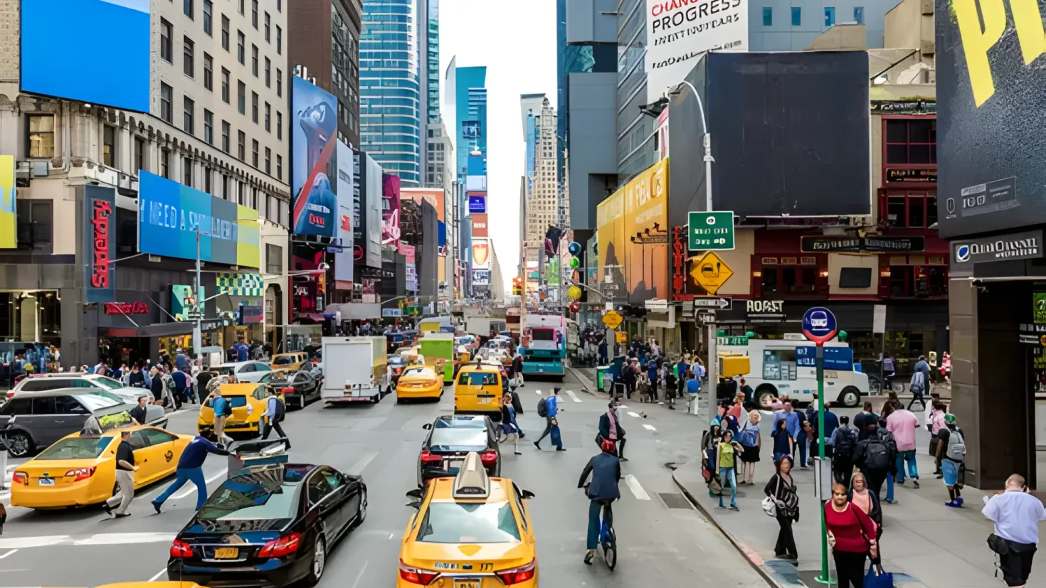 A bustling city street filled with lots of traffic, including cars, buses, and people walking on the footpath. There are also sign boards, street poles, street lights, and buildings with windows lining the street. The sky is visible in the background.