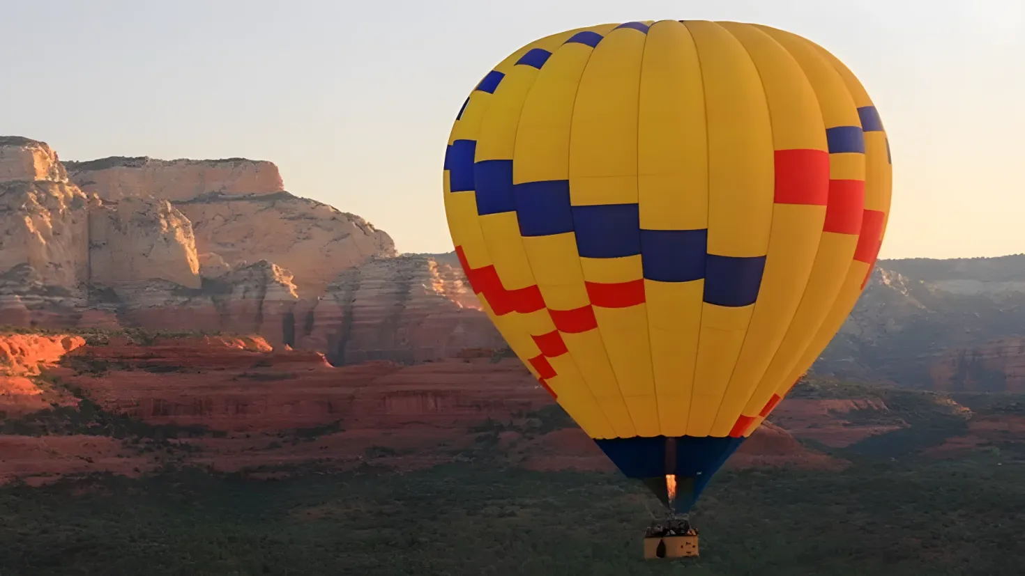 A hot air balloon flying over a desert landscape with hills in the background and a clear blue sky above.