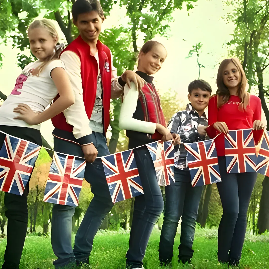 A family of five standing in the grass, each holding a British flag. The background of the image is filled with trees and a clear blue sky.
