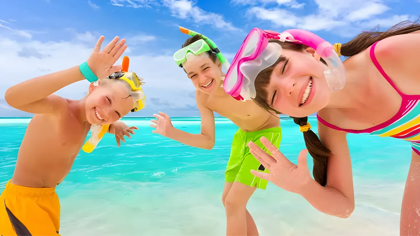 Three children wearing snorkeling gear on the beach, with the sky and clouds in the background. They are all smiling and appear to be enjoying the sun and the sound of the waves crashing against the shore.